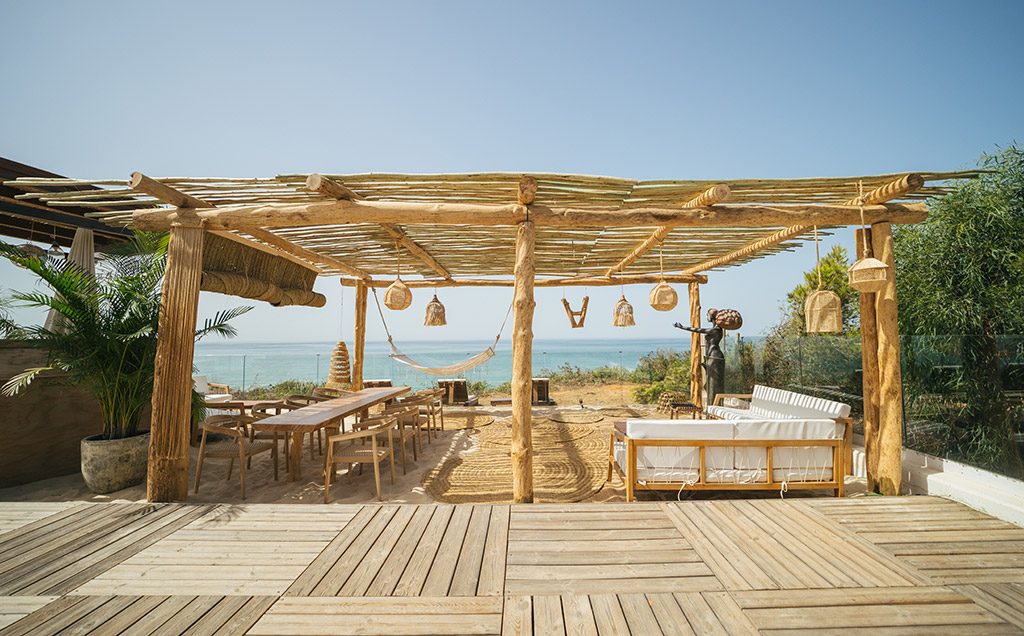Zona chill-out bajo pérgola de madera en Atenas Playa, frente al mar